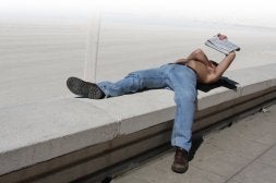Un joven lee un periódico mientras toma el sol en el Paseo Marítimo de Almería, hace unos días./